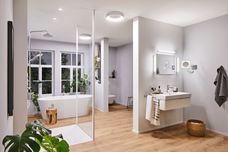 Helles Badezimmer mit freistehender Badewanne, begehbarer Dusche, wandhängendem Waschtisch und runden Deckenleuchten auf Boden in Holzoptik.
