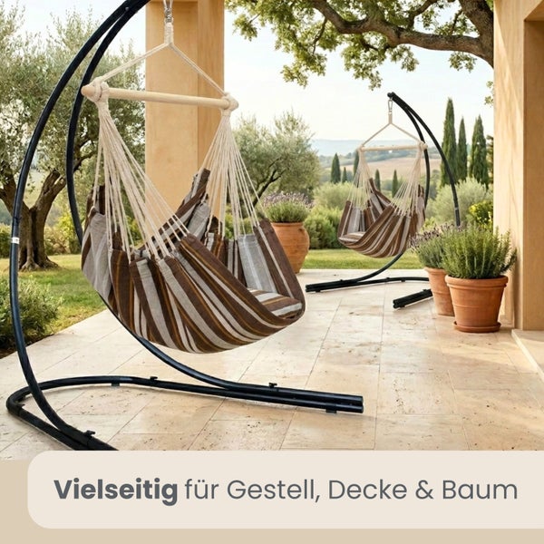 Gestreifte Hängesessel mit Holzstab an Metallgestellen auf einer Terrasse mit Olivenbäumen und Pflanzen.