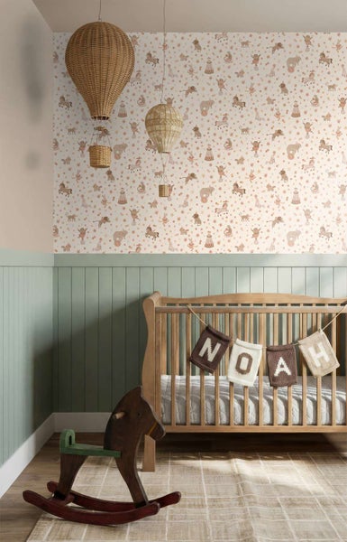 Kinderzimmer mit Zirkus Tapete, hängenden Rattan Heißluftballons, Holzgitterbett mit Namensgirlande und einem Schaukelpferd aus Holz.