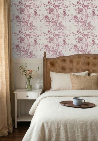 Schlafzimmer mit Mustertapete mit Vogelmotiven und Zweigen, Bett mit Kopfteil aus Wiener Geflecht und weißem Nachttisch mit Blumen.