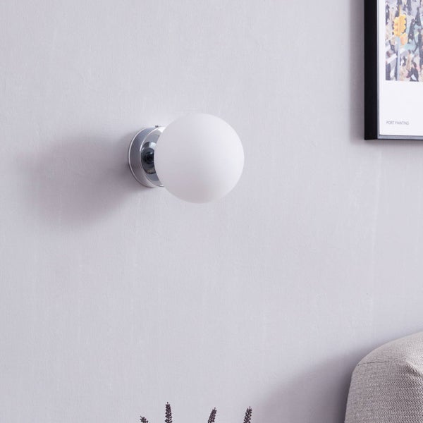 Moderne Wandleuchte mit weißem kugelförmigem Glasschirm und Metallfuß an einer hellen Wand in einem minimalistischen Raum.