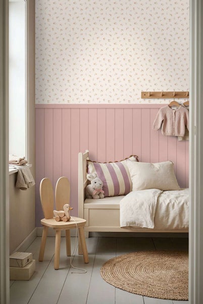 Kinderzimmer mit blumiger Tapete und rosa Wandverkleidung, Bett, Holzstuhl und Jute Teppich.