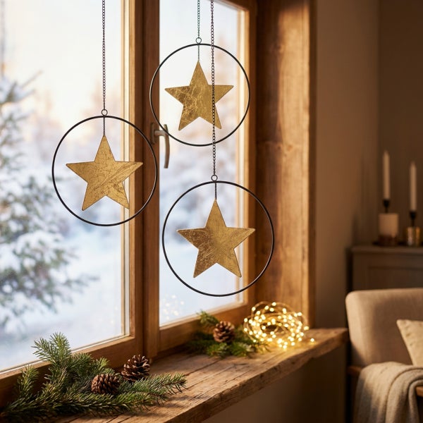 Drei dekorative Weihnachtssterne in Metallringen zum Aufhängen vor einem Fenster mit winterlicher Dekoration aus Tannenzweigen und Lichterkette.