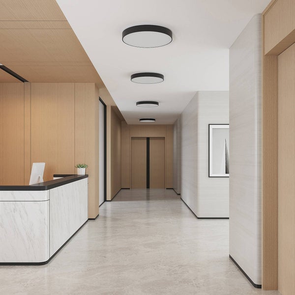 Moderner heller Flur mit runden schwarzen Deckenlampen, einem Empfangstresen in Marmoroptik und Wandverkleidungen aus Holz.