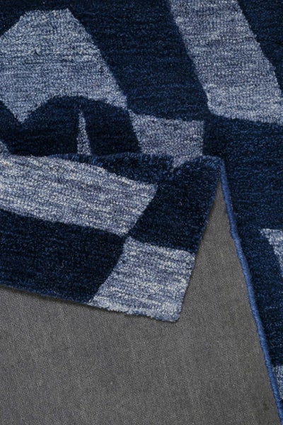 Teppich mit geometrischem Muster in Blau und Grau, Hochflor, Detailansicht mit umgeschlagener Ecke.