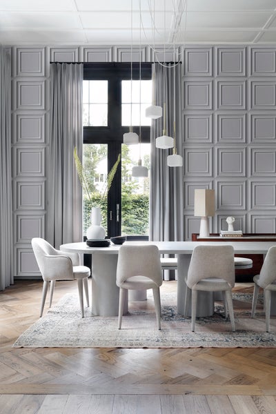 Heller Essbereich mit ovalem Tisch, Stühlen und Pendelleuchten vor einer Wand mit Kassettenpaneelen.