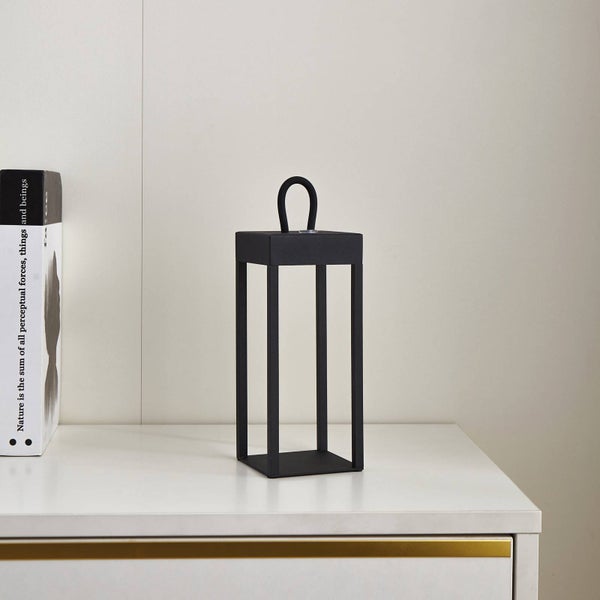Moderne schwarze Metalllaterne mit rechteckigem Rahmen auf einer weißen Oberfläche neben einem Buch.