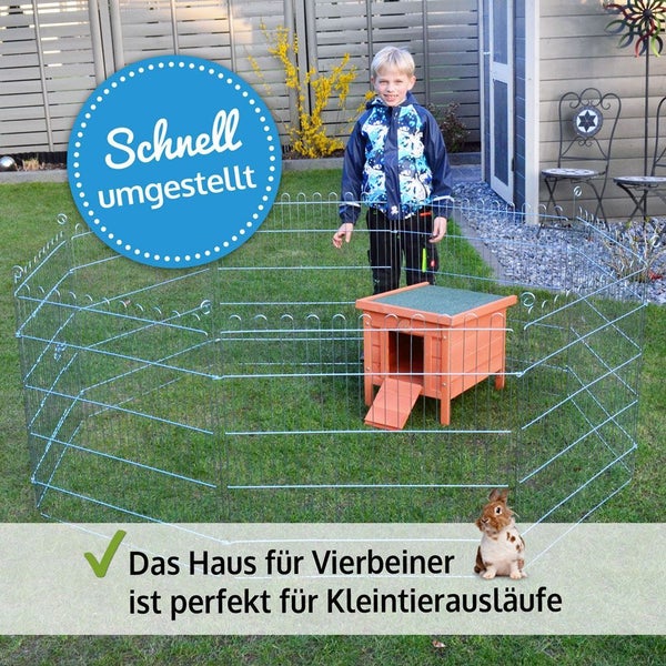 Hölzernes Kleintierhaus mit Metall-Freigehege auf einer Rasenfläche im Garten mit einem Kaninchen und einem Kind im Hintergrund.