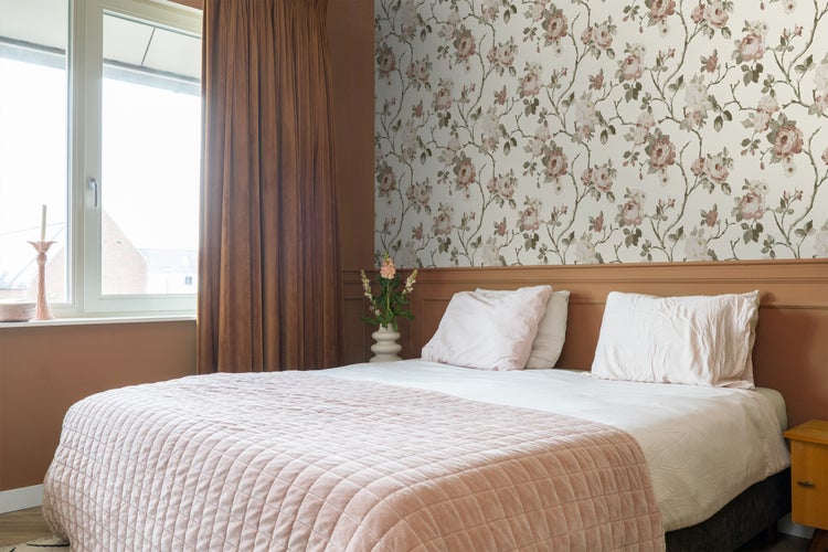 Schlafzimmer mit Doppelbett, Blumenvliestapete und braunen Vorhängen