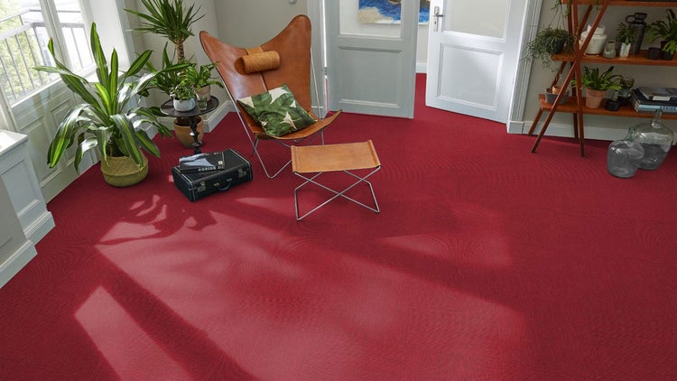 Rote Teppichfliesen in einem hellen Wohnzimmer mit Ledersessel und Zimmerpflanzen.