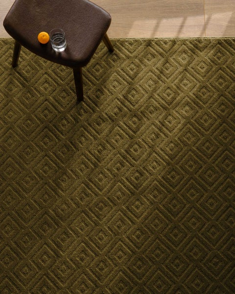Teppich mit geometrischem Quadratmuster auf Holzboden, weiche Textur, neben einem Buch und Kissen.