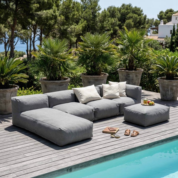 Modulares graues Outdoor-Sofa auf einer Holzterrasse am Pool, umgeben von Palmen in großen Töpfen.