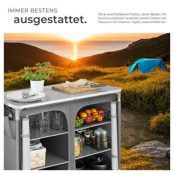 Campingküche mit Geschirr, Töpfen und Lebensmitteln vor malerischer Landschaft mit Zelt