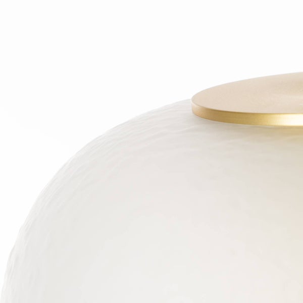 Dreiflammige Pendelleuchte mit weißen Schirmen und Messingdetails über einem Tisch in einem hellen, modernen Raum.