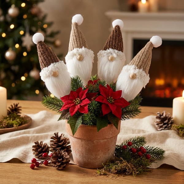 Weihnachtsgesteck in Terrakottatopf mit vier Wichtelfiguren, Poinsettien und Tannenreisig auf einem Holztisch vor einem Kamin.