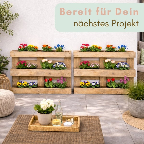 Zwei vertikale Pflanzregale aus Holzpaletten mit Blumen auf einer Terrasse neben einem Rattantisch.