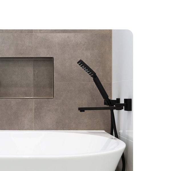 Moderne Badewannenarmatur in Schwarz matt mit Handbrause an einer Wand mit großformatigen Fliesen in Natursteinoptik über einer weißen Badewanne.