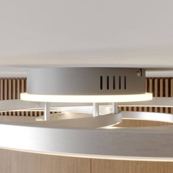 Moderne LED-Deckenleuchte mit warmweißen, ringförmigen Elementen und einem zylindrischen Sockel vor einer Holzwand.