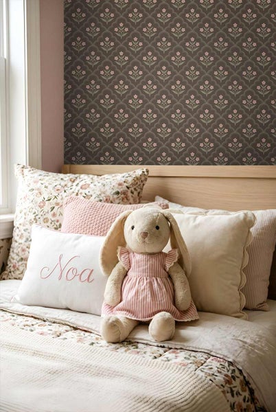 Kinderzimmer mit gemusterter Blumentapete an der Wand, helles Holzbett mit verschiedenen Dekokissen und einem Stoffhasen.