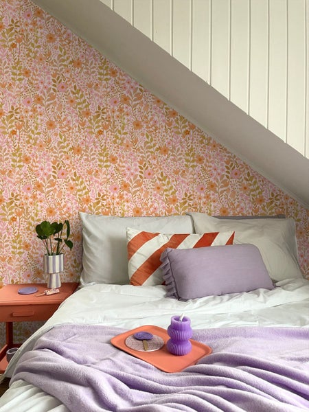 Ein Schlafzimmer unter einem Dachschrägenfenster mit einem Bett, Kissen, Decken, Nachttisch und dekorativer Blumenvliestapete.