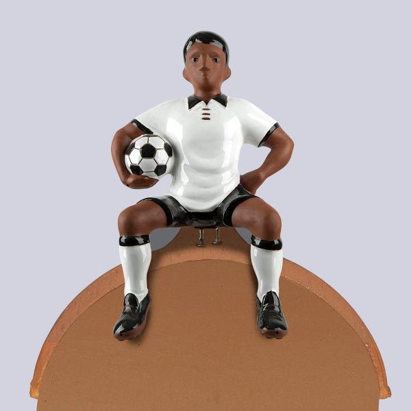 Keramik-Figur eines Fußballers, sitzend auf einem braunen Sockel mit einem Fußball unter dem Arm.