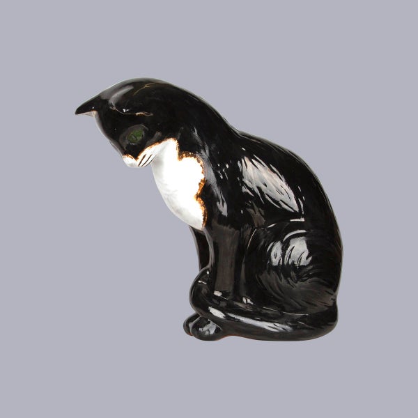 Dekorative Katzenfigur aus Keramik, sitzend und nach unten blickend, schwarz und weiß, glänzend.