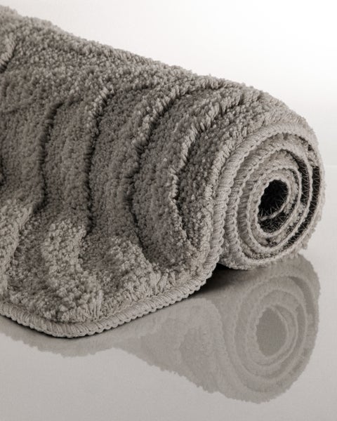 Zusammengerollte Badematte mit Hochflor-Textur und Wellenmuster.