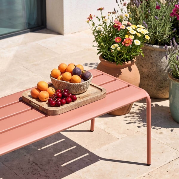 Moderner Metall-Beistelltisch mit Lattenoberfläche auf einer Terrasse, dekoriert mit einer Obstschale und Blumen im Hintergrund.
