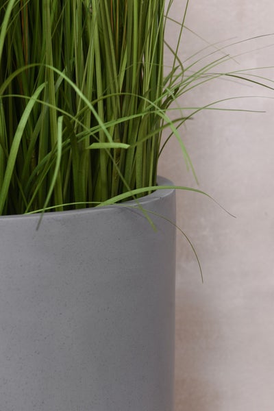 Detailansicht von künstlichem Gras in einem grauen zylindrischen Pflanztopf mit Steinoptik.