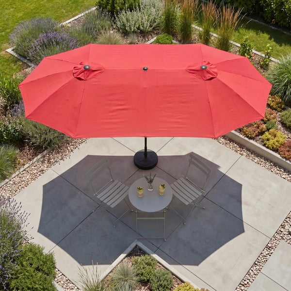 Großer roter Doppel-Sonnenschirm über einer Sitzgruppe aus Metall auf einer modernen Terrasse, umgeben von einem Garten.