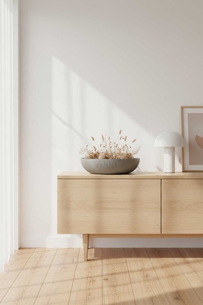 Minimalistisches Sideboard aus Holz in hellem Raum mit Dekoschale mit Trockenblumen und einer Tischlampe.
