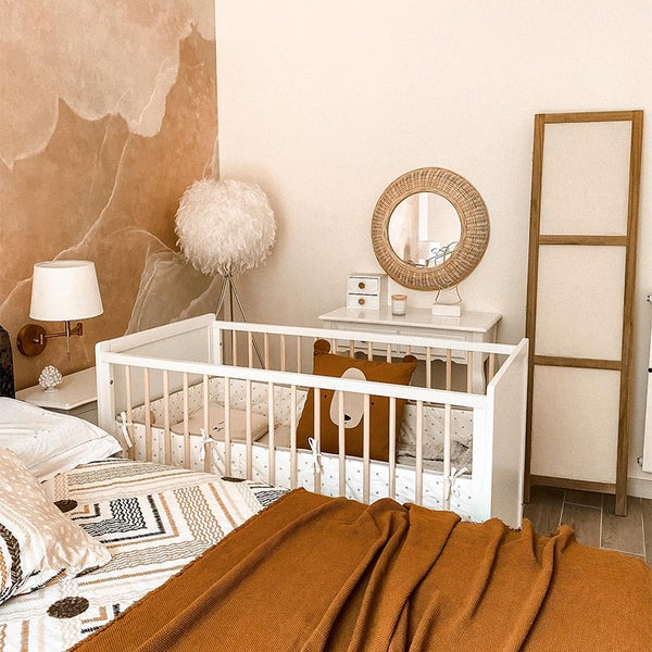 Ein Kinderzimmer mit Kinderbett, Kommode, Spiegel, Lampe und dekorativen Kissen.