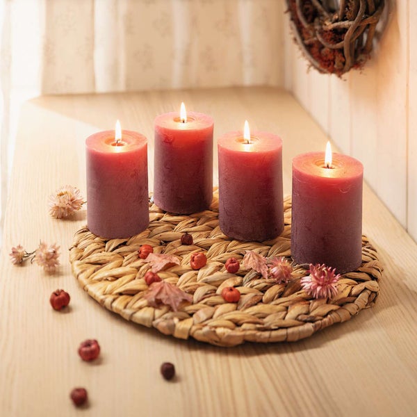 Dekorative Anordnung mit vier Stumpenkerzen auf einem Tisch mit Herbstdekoration.