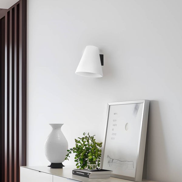 Moderne weiße Wandleuchte in konischer Form über einem Sideboard mit einer Vase, einer Pflanze und einem gerahmten Bild in einem hellen Zimmer.