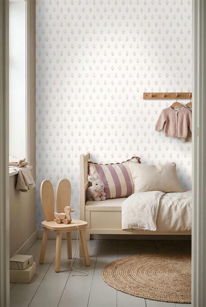Helles Kinderzimmer mit floral gemusterter Tapete, einem Holzbett mit Kissen, einem Kinderstuhl in Hasenform und einem runden Jute-Teppich.