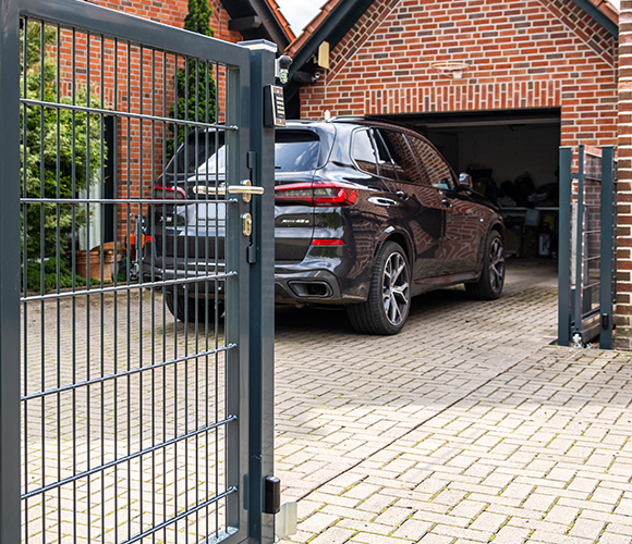 Einfahrtstor aus Metall vor einem Wohnhaus mit Garage und Auto