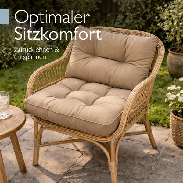 Garten-Loungesessel aus Rattan mit dicken Polstern auf einer hellen Steinterrasse im Garten.