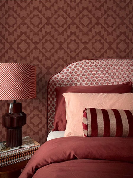 Schlafzimmer mit Vliestapete mit geometrischem Muster, gepolstertem Kopfteil, Bettwäsche und Tischlampe im modernen Einrichtungsstil.