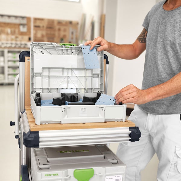 Handwerker entnimmt Schleifpapier aus einem Werkzeugkoffer auf einem Werkstattwagen