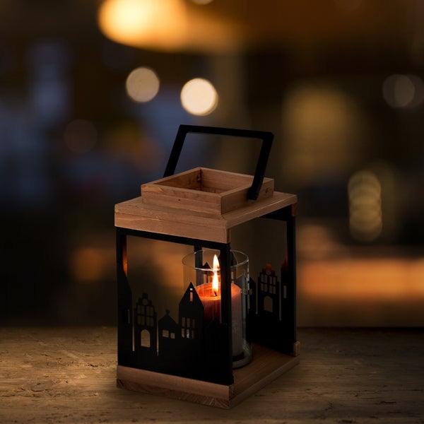 Holzlaterne mit Häusersilhouette aus schwarzem Metall und brennender Kerze im Glaszylinder.