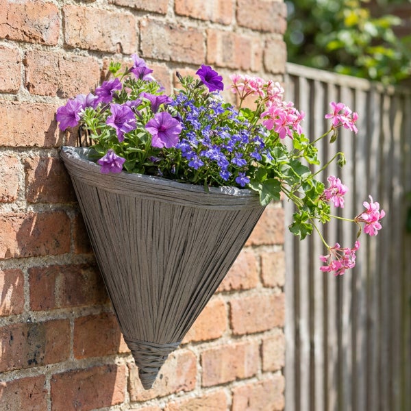 Konischer Wandpflanzkorb bepflanzt mit Blumen an einer Ziegelmauer