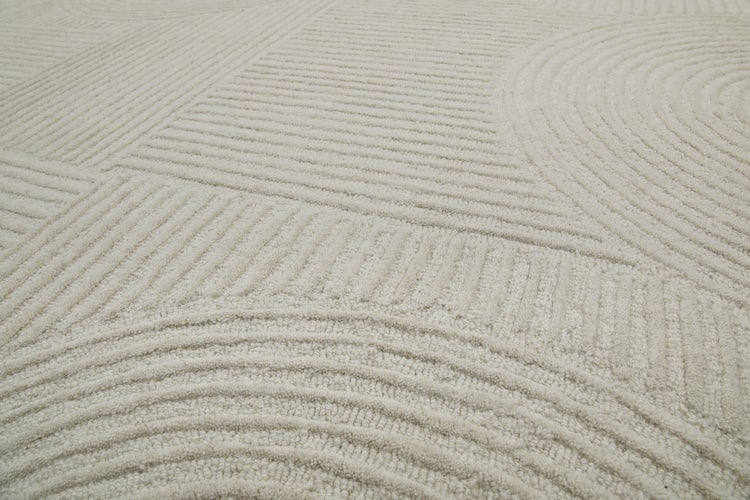 Detailaufnahme eines Teppichs mit Hoch-Tief-Struktur und einem geometrischen Muster aus Linien und Kreisformen.