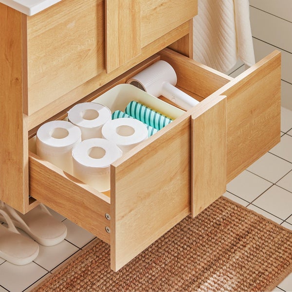 Offene Schublade eines Badezimmerschranks mit Toilettenpapier, Haartrockner und Accessoires.