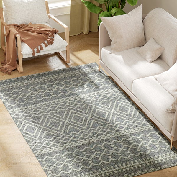 Rechteckiger Teppich mit grauem geometrischem Muster in einem hellen Wohnzimmer mit Sofa und Sessel auf Holzboden.