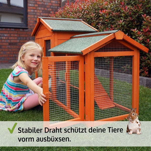 Kleintierstall aus Holz mit stabilem Drahtgeflecht und Bitumendach im Garten. Kind öffnet das Gittertor, daneben ein Kaninchen.