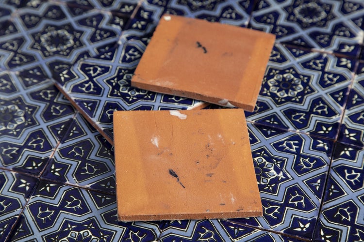 Zwei quadratische Fliesen liegen auf einem blauen Fliesenmuster.