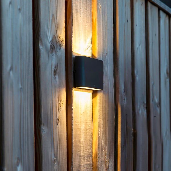 Schwarze LED-Außenwandleuchte mit Up-and-Down-Lichteffekt an einem Holzzaun.