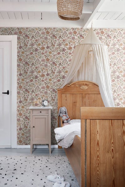 Kinderzimmer mit floral gemusterter Tapete, einem Naturholzbett mit weißem Betthimmel und einem kleinen Nachttisch.