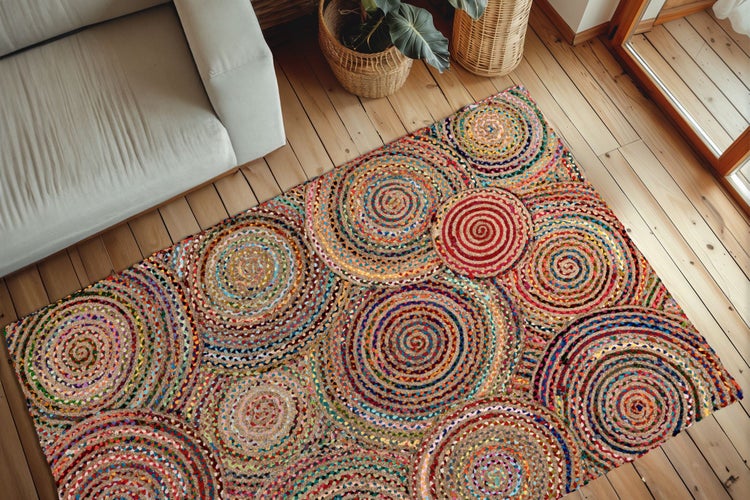 Bunter geflochtener Teppich mit kreisförmigem Muster im modern eingerichteten Wohnzimmer mit hellem Sofa und Holzmöbeln.