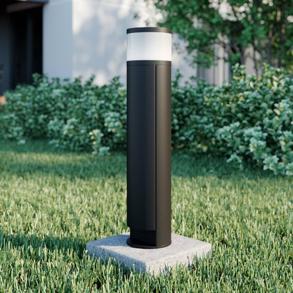Moderne zylindrische Wegeleuchte aus Metall auf einem Steinsockel im Rasen vor einer Hecke im Garten.